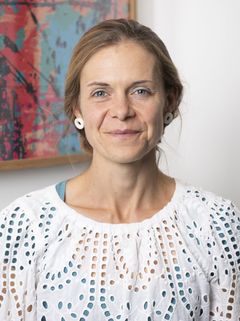 Caroline Taunt smiling, wearing a white top in front of a colourful painting