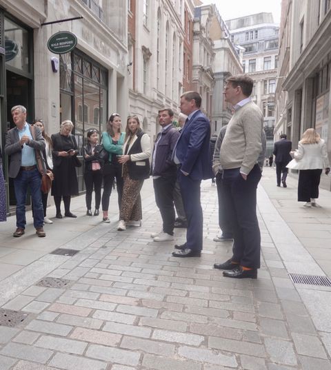 A walking group pauses on a pedestrianised City street lined with stone office buildings