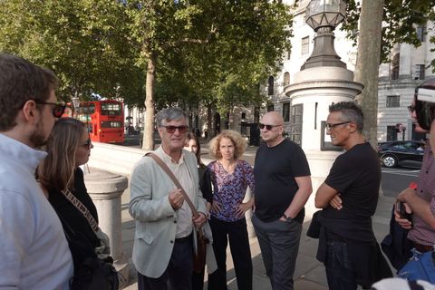 Conference delegates gather around a guide on a Westminster street corner as a red London bus passes behind them
