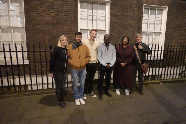 A small group of Virgin colleagues and their guide pose outside a Georgian brick terrace in Soho after dark