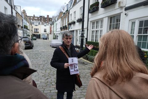 A guide holds up an archive photograph as he tells guests the history of a cobbled Belgravia mews