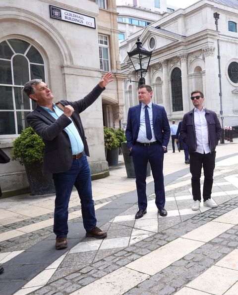 A guide points up at a building on Guildhall Buildings while two walkers look on