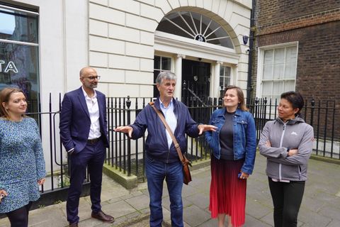 A guide gestures as he talks to a small group outside a Georgian doorway on a Soho street