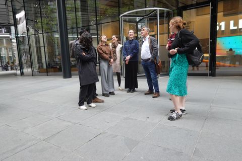 A guide meets a small group of colleagues outside the glass entrance of their City of London office before a lunchtime walk