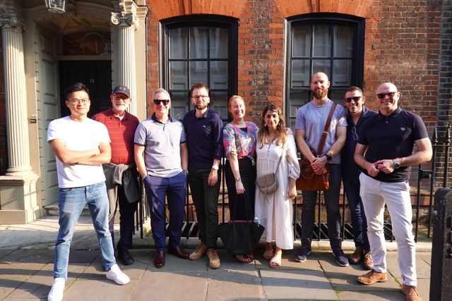 A smiling team poses for a photo outside a Georgian townhouse in Spitalfields on a sunny evening walk