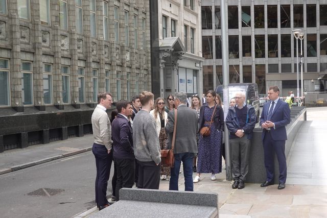 Colleagues in business dress gather around a guide on a quiet City of London street
