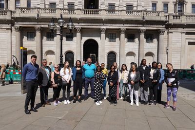 A large team on a wellbeing walk lines up for a photo outside the Bank of England on a sunny day